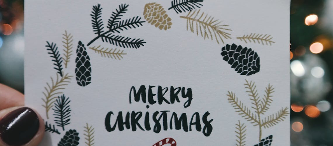 Merry Christmas card held in front of decorative tree with bokeh lights.