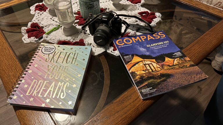 a sketchbook laying on the table with a magazine and camera